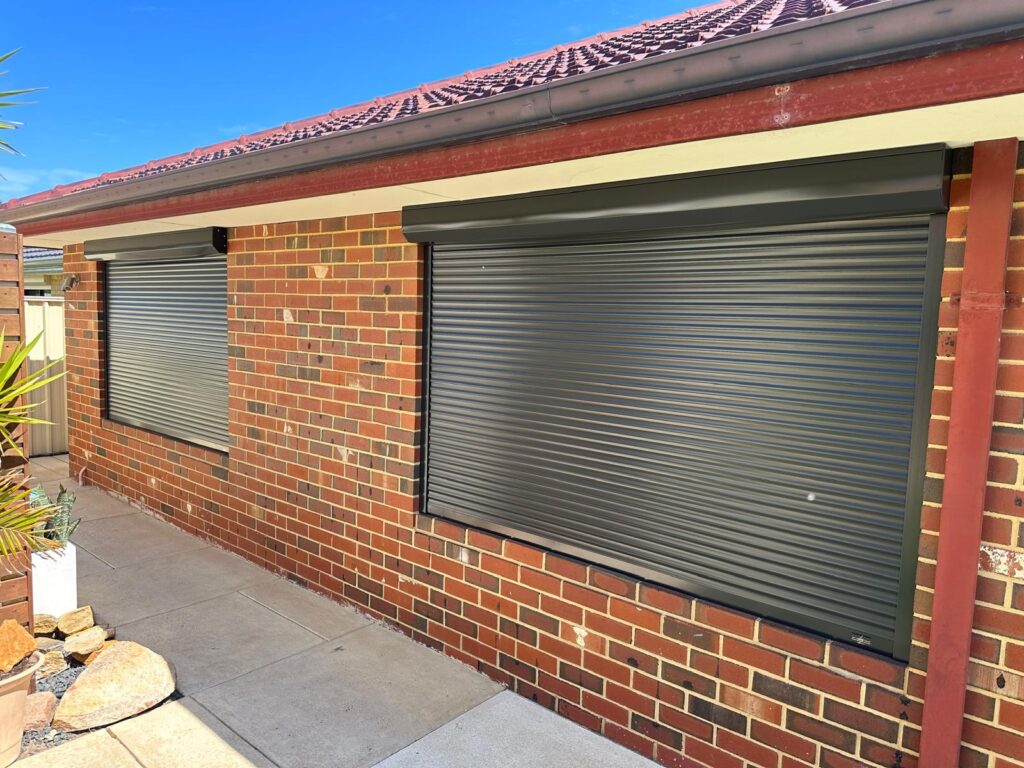 Charcoal roller shutters fully closed on brick home-manual vs electric both provide full blockout.