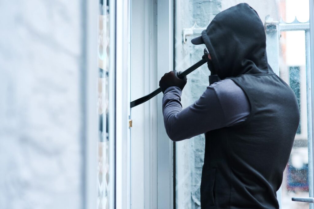 A masked burglar using a crowbar to force entry, representing the high financial risks of commercial break-ins.